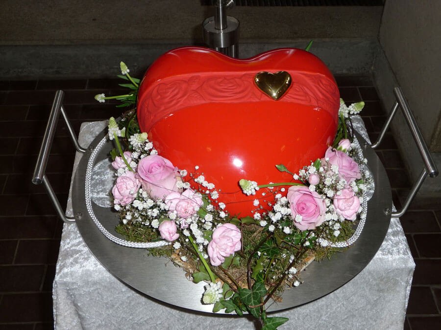 Bestattungsvorsorge Bad Oeynhausen | Rote Urne in Herzform dekoriert mit rosaen Rosen