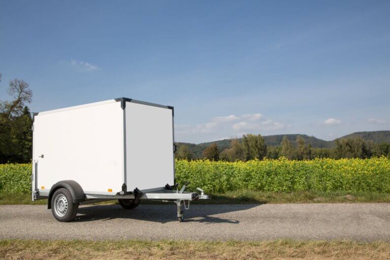 Anhänger mit Plane steht vor einer Wise auf der Straße