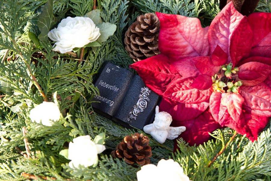 Bestattungsvorsorge Garbsen | Ein liebevoll gestaltetes Grabgesteck mit Weihnachtsstern, weißen Ranunkeln und einer Gedenktafel spendet Trost in der kalten Jahreszeit und hält die Erinnerung an Verstorbene wach