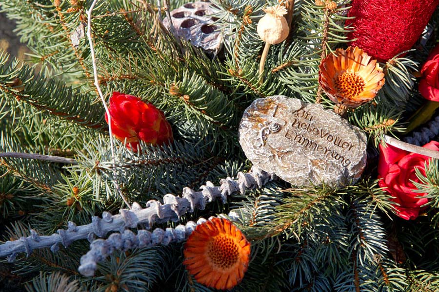 Bestattungsvorsorge Garbsen | Ein Gedenkstein mit der Aufschrift „In liebevoller Erinnerung“, eingebettet in ein winterliches Trauergesteck aus Tannenzweigen und Trockenblumen, symbolisiert bleibende Verbundenheit mit dem Verstorbenen