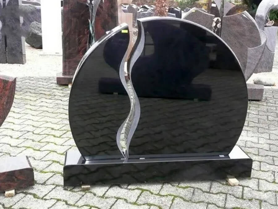 Steinmetzbetrieb und Grabmale Rinteln | Schwarzer Granit-Grabstein in runder Form mit geschwungenem Dekorelement auf passendem Sockel