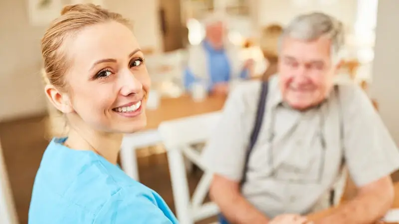 Altenpflege Oldenburg | Lächelnde Pflegehilfe hält Hand vom Senior
