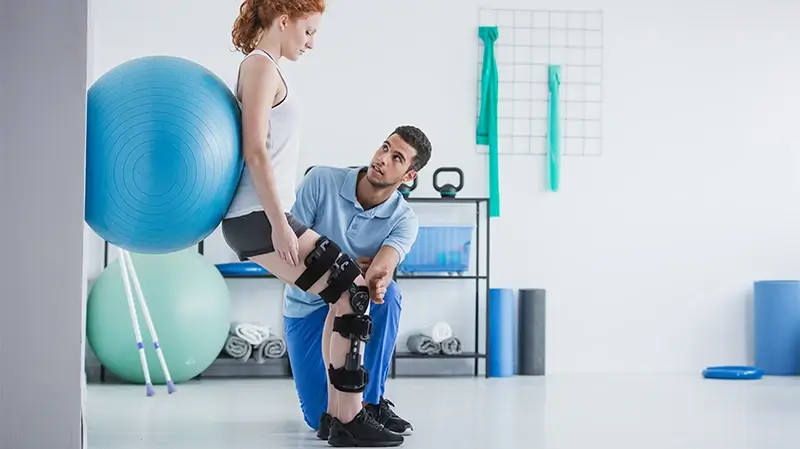 Physiotherapeut unterstützt eine Patientin, mit orthopädischem Problem, bei einem Training mit einem Ball Physiotherapie in Nortorf | Physiotherapeut unterstützt eine Patientin