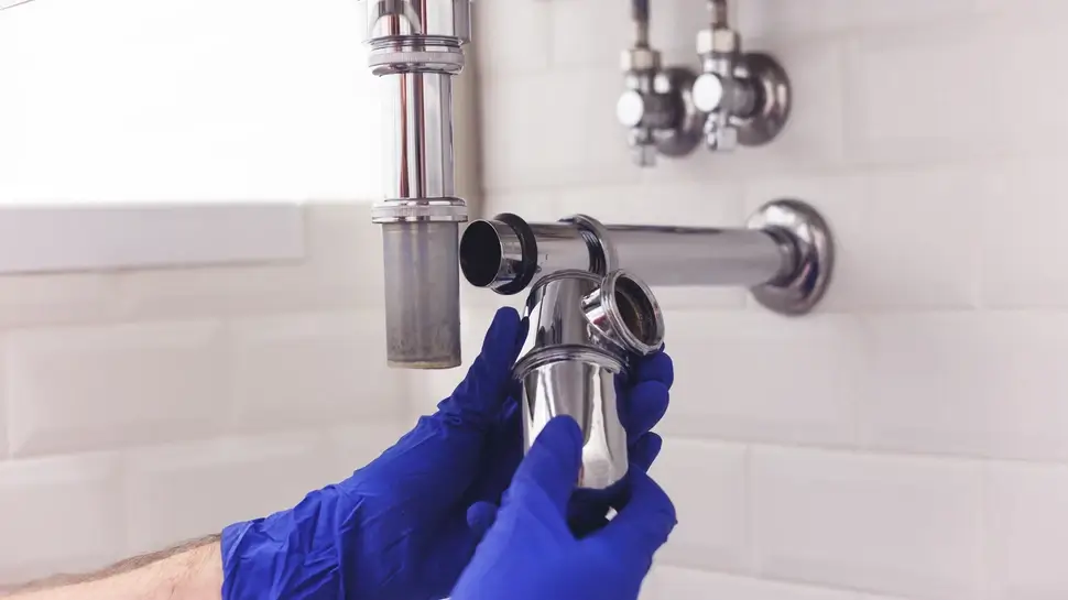 Plumber repairs and maintains chrome siphon under the washbasin. Plumber at work in bathroom, plumbing assemble and install concept Rohrreinigungsservice Havixbeck | Installateur wechselt Siphon