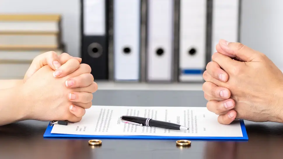 Familienrecht Husum 2 Familienrecht Husum | Gefaltete Hände des Noch-Ehepaares auf Scheidungsvertrag. Davor die Eheringe