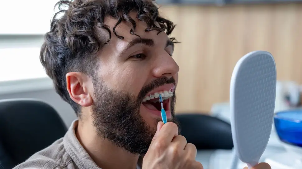 Man with metal braces carefully cleaning his teeth using interdental brush Kieferorthopädin Lübeck | 
Reinigung mit fester Zahnspange
