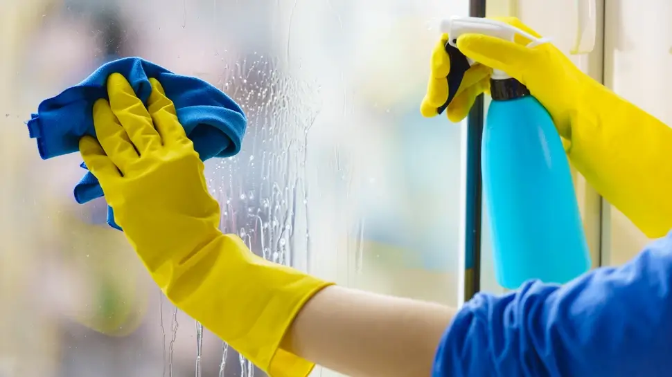 Gloved hand cleaning window rag and spray Fensterreinigung Meppen | Nahaufnahme Fensterputzen