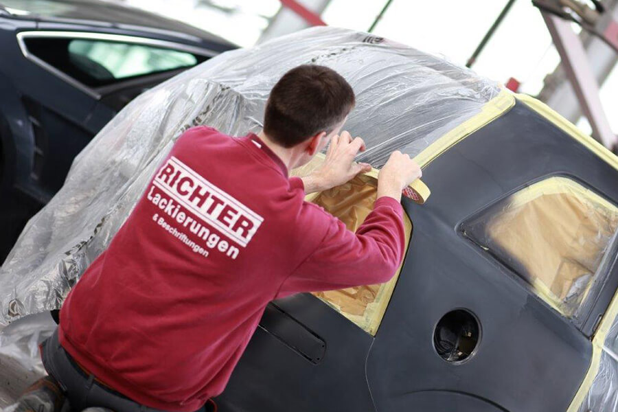 Unfallinstandsetzung von Fahrzeugen und Fahrzeuglackierungen in Coesfeld | Ein Mitarbeiter der Richter Lackierungen GmbH beim Abkleben eines Autos