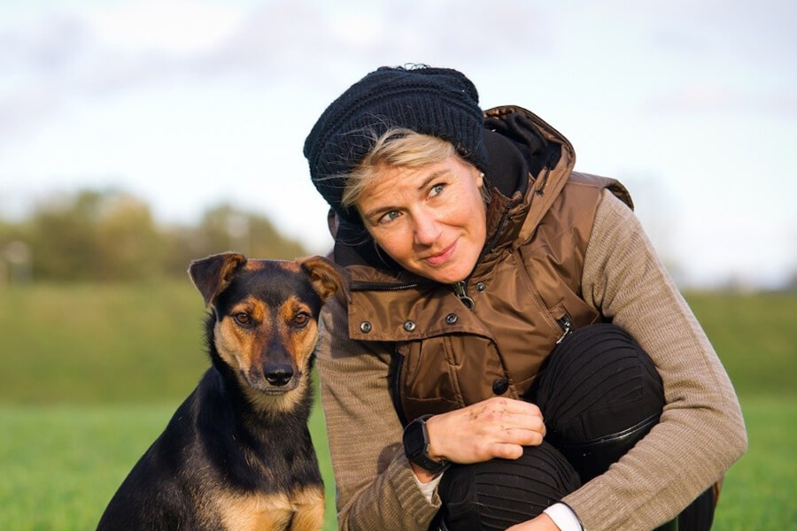 Tierbestatter Bonn | Eine Frau schaut zusammen mit ihrem Hund in die Ferne, auf einer grüünen Wiese