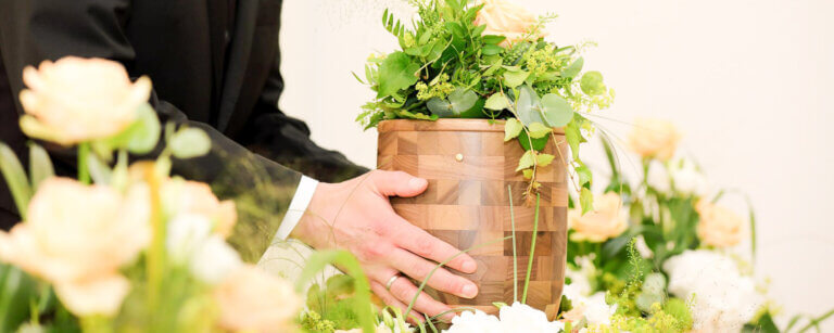 Bestattungsvorsorge Lilienthal | Holzurne mit Blumenarrangement bei einer Trauerfeier