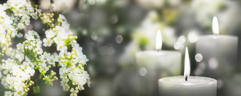 Bestattungsvorsorge Uplengen | Weiße Blüten und brennende Kerzen als Symbol für Trauer und stille Erinnerung