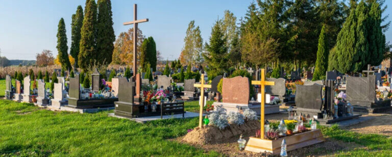 Bestattungsvorsorge Esens | Friedhof mit frisch angelegtem Grab, Holzkreuz und umliegenden Grabsteinen in einer ruhigen Umgebung