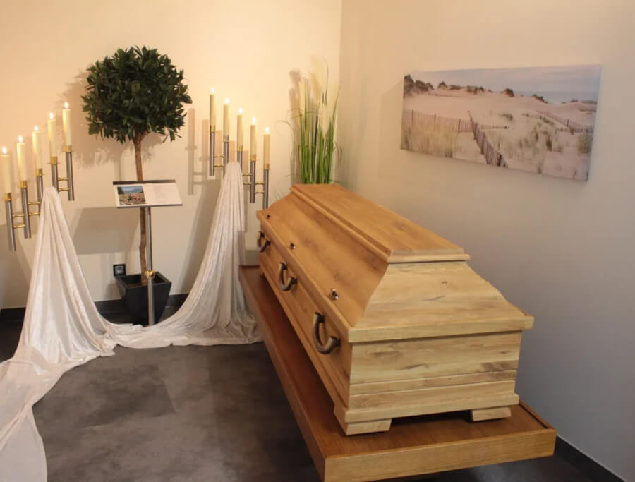Bestattungsvorsorge Esens | Abschiedsraum der Onno Haak GmbH mit hellem Holzsarg, Kerzenleuchtern und schlichter Dekoration, ideal für eine würdevolle Trauerfeier