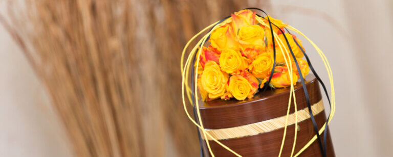 Bestattungsarten in Göttingen | Eine stilvolle Urne mit gelben Rosen als Ausdruck von Wertschätzung und Würde in der Abschiedsgestaltung