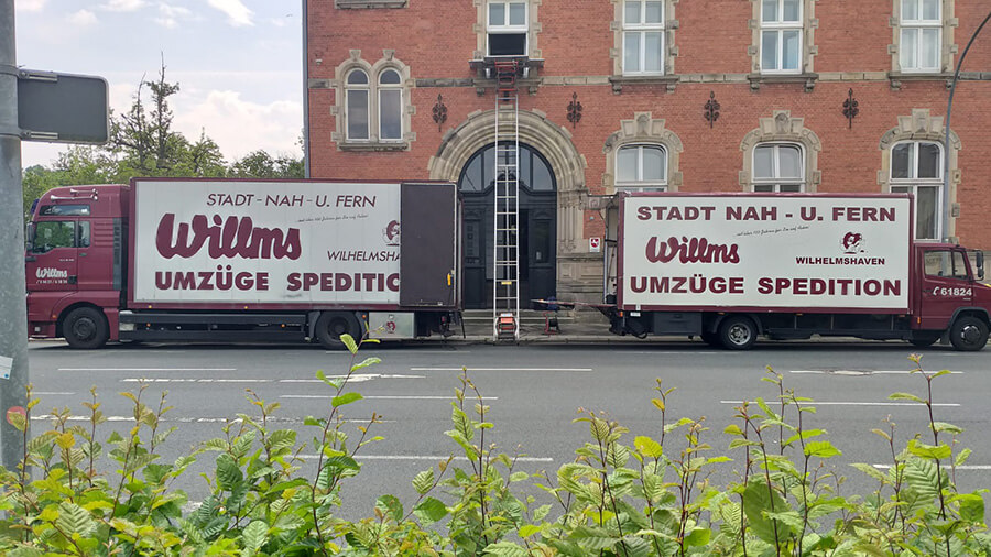 Umzüge in Wilhelmshaven | Zwei Umzugsfahrzeuge der Willms Spedition vor einem historischen Gebäude, bereit für einen reibungslosen Privatumzug