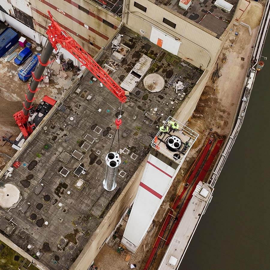 Schornsteintechnik Oberhausen | Auch industrielle Großprojekte werden mit millimetergenauer Planung realisiert – hier wird ein Edelstahl-Schornsteinmodul per Schwerlastkran auf einem Kraftwerksgebäude eingehoben